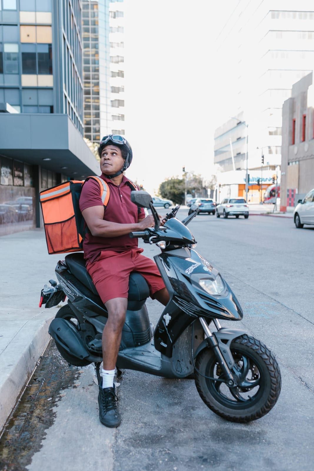 A delivery rider on a scooter with an orange delivery bag